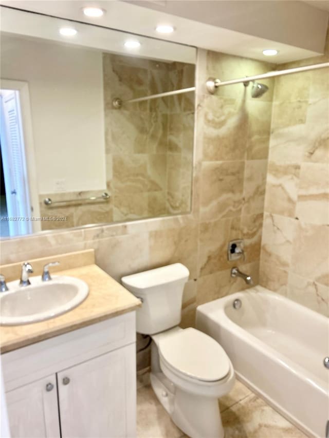 full bathroom featuring tile patterned floors, toilet, tiled shower / bath, tile walls, and vanity