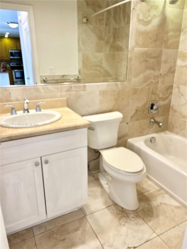 full bathroom featuring toilet, tile patterned floors, tile walls, tiled shower / bath, and vanity