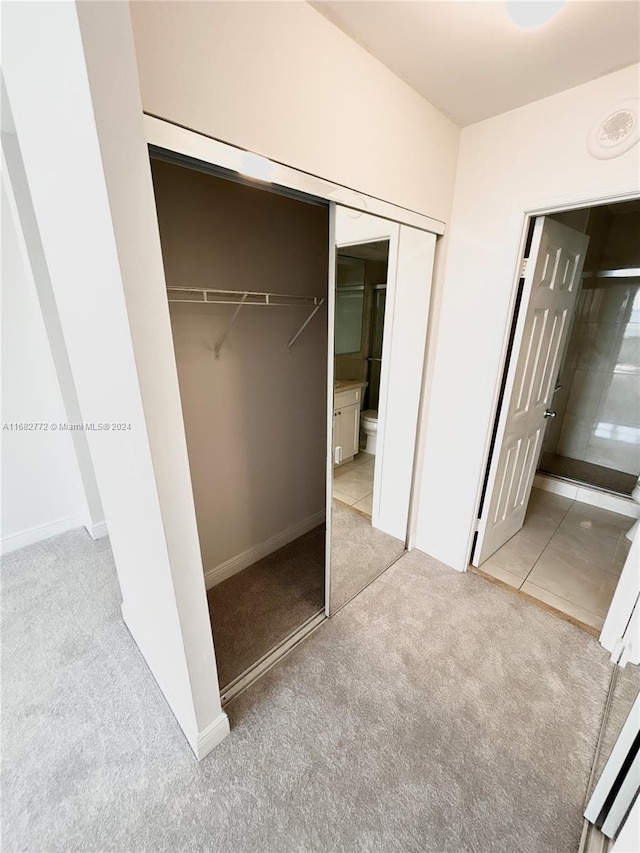 unfurnished bedroom with a closet, light colored carpet, and connected bathroom