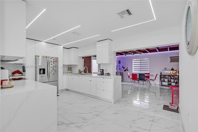 kitchen featuring sink, light stone counters, stainless steel fridge with ice dispenser, and white cabinets