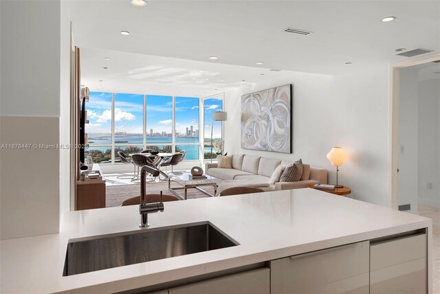 kitchen with white cabinets, a water view, expansive windows, and sink