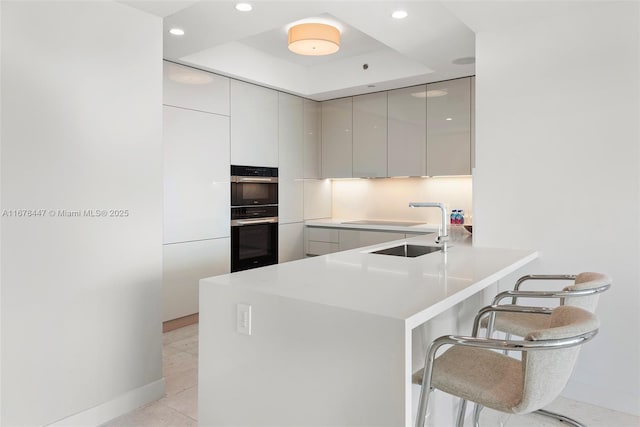 kitchen featuring a breakfast bar, a raised ceiling, sink, double oven, and kitchen peninsula