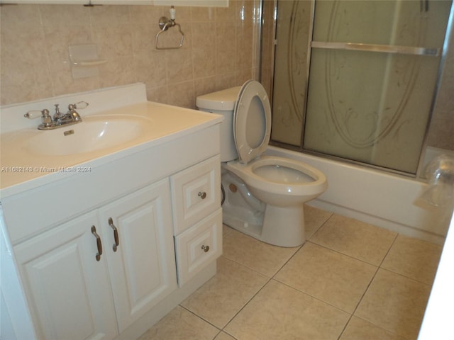 full bathroom with combined bath / shower with glass door, tile walls, toilet, vanity, and tile patterned floors