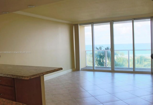 spare room with crown molding, light tile patterned floors, a water view, expansive windows, and baseboards