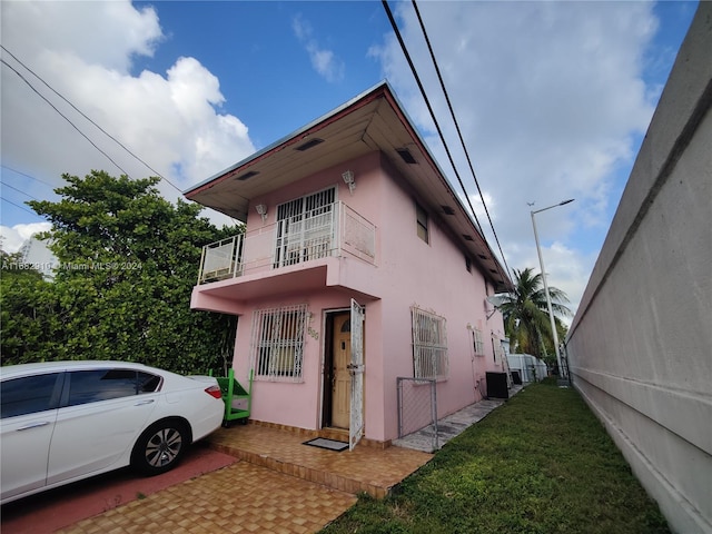 view of side of property with a balcony, a yard, and central air condition unit