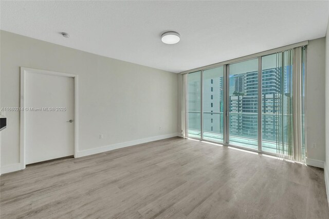 empty room with a wall of windows, a textured ceiling, and light wood-type flooring