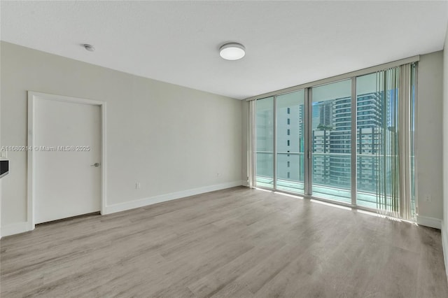 empty room with a wall of windows, a textured ceiling, and light wood-type flooring