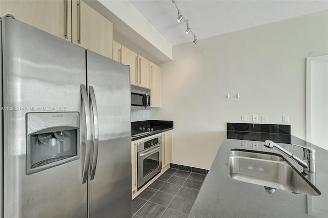 kitchen featuring light brown cabinetry, sink, dark tile patterned floors, stainless steel appliances, and a textured ceiling