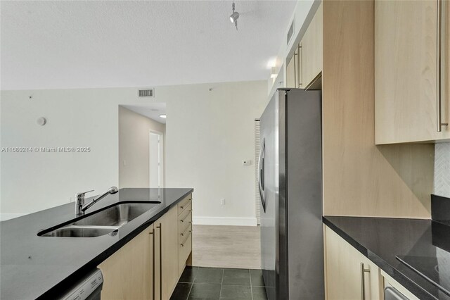 kitchen featuring black dishwasher, sink, stainless steel fridge, dark tile patterned flooring, and light brown cabinets