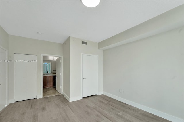 unfurnished bedroom with ensuite bath and light hardwood / wood-style floors