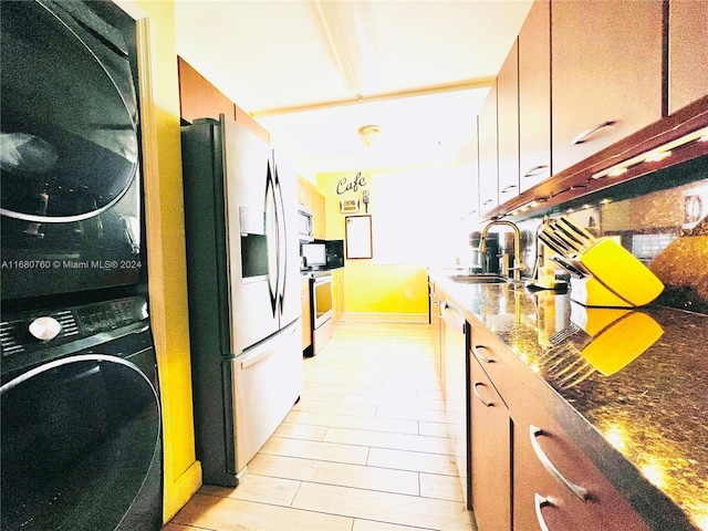 kitchen featuring stone countertops, stainless steel appliances, stacked washer / dryer, and sink