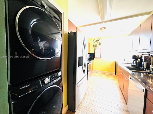 kitchen with stacked washer and clothes dryer, sink, light hardwood / wood-style flooring, dark stone countertops, and appliances with stainless steel finishes