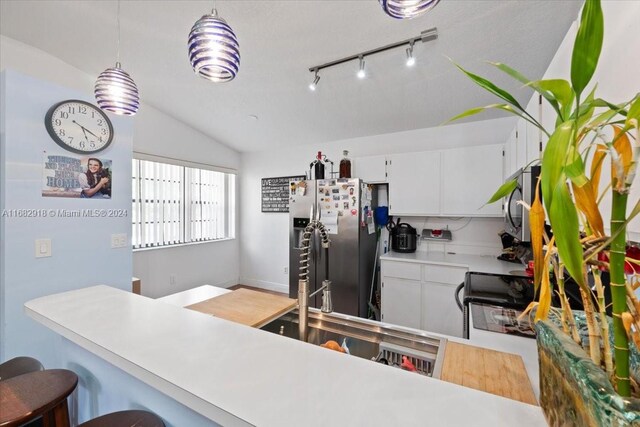 kitchen featuring hanging light fixtures, stainless steel appliances, vaulted ceiling, a kitchen bar, and white cabinets