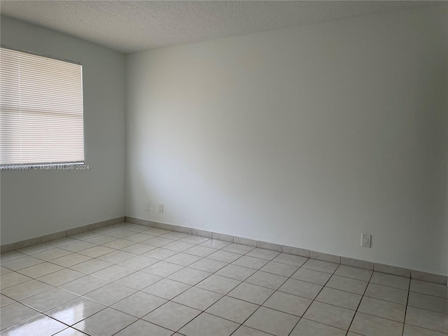 empty room with a textured ceiling and light tile patterned floors