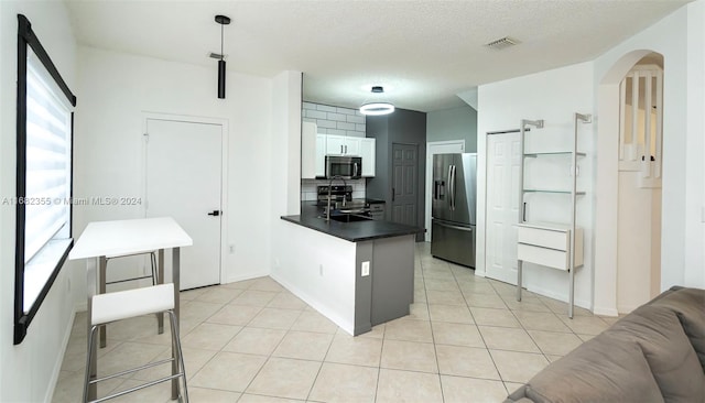 kitchen with kitchen peninsula, white cabinets, tasteful backsplash, a textured ceiling, and stainless steel appliances