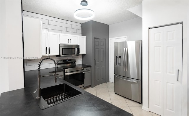 kitchen with white cabinets, appliances with stainless steel finishes, a textured ceiling, light tile patterned flooring, and sink