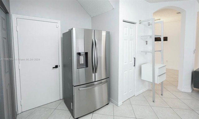 kitchen with vaulted ceiling, light tile patterned flooring, and stainless steel fridge