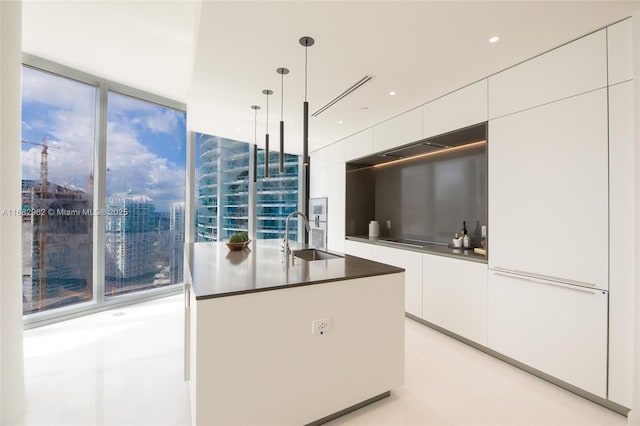 kitchen with black electric stovetop, floor to ceiling windows, sink, white cabinets, and hanging light fixtures