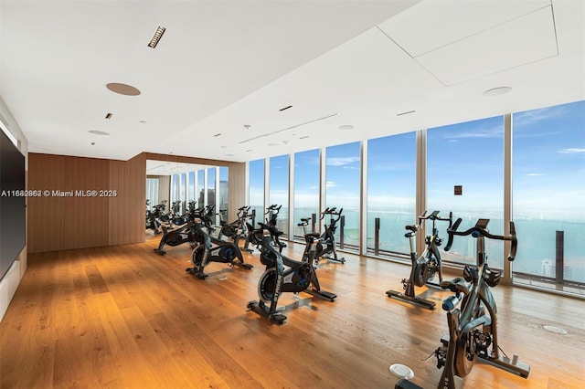 workout area with a wall of windows, a water view, and hardwood / wood-style flooring