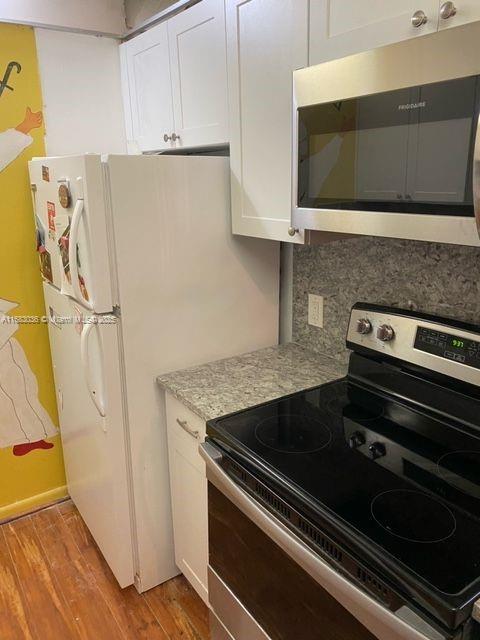 kitchen featuring backsplash, stainless steel appliances, light wood-type flooring, and white cabinets