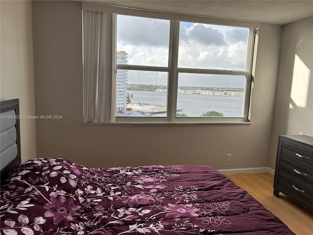 bedroom featuring a textured ceiling, a water view, and light wood-type flooring