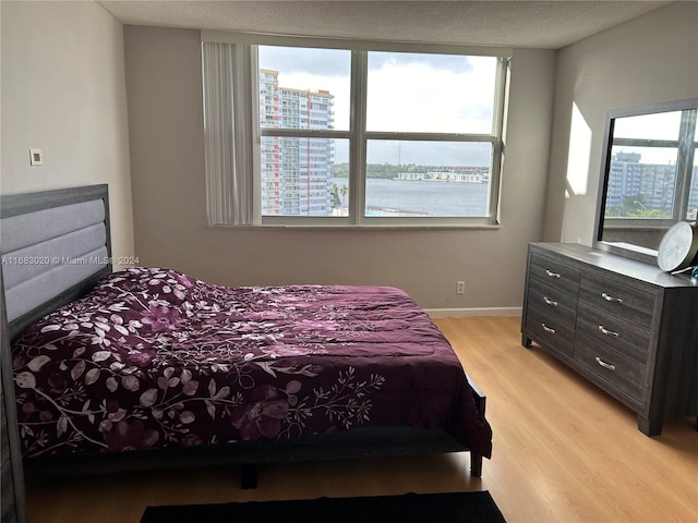 bedroom with a water view, light hardwood / wood-style flooring, multiple windows, and a textured ceiling