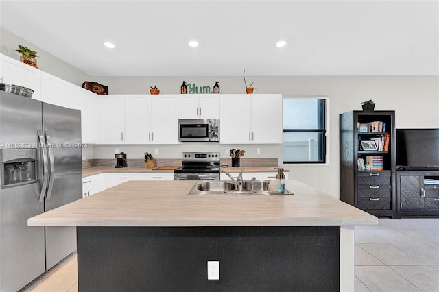 kitchen with sink, appliances with stainless steel finishes, light tile patterned floors, an island with sink, and white cabinets