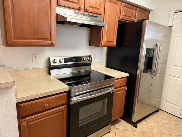 kitchen featuring brown cabinetry, light countertops, under cabinet range hood, light tile patterned floors, and stainless steel appliances