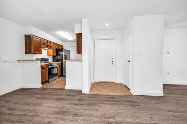 kitchen featuring baseboards, light wood-style floors, light countertops, under cabinet range hood, and stainless steel appliances