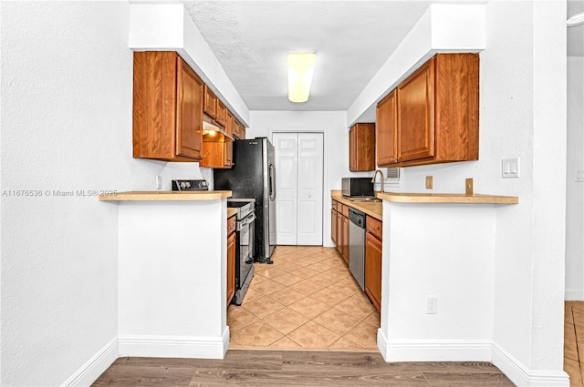 kitchen featuring light countertops, brown cabinetry, stainless steel appliances, baseboards, and light wood-type flooring