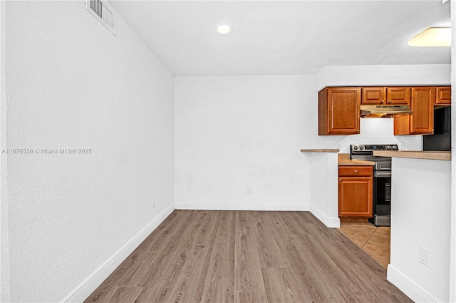 kitchen with visible vents, light countertops, wood finished floors, under cabinet range hood, and stainless steel electric stove