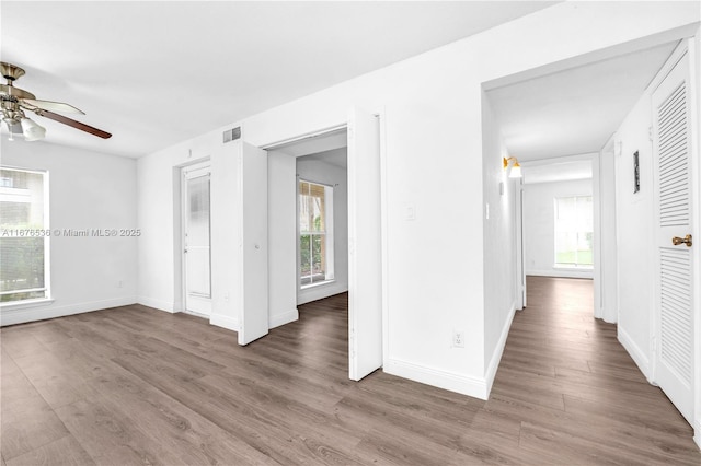 empty room with a ceiling fan, visible vents, a wealth of natural light, and wood finished floors