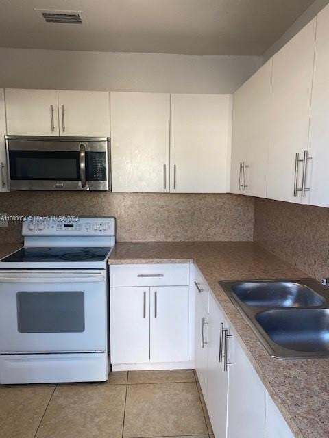 kitchen featuring white electric range oven, sink, white cabinets, and light tile patterned flooring