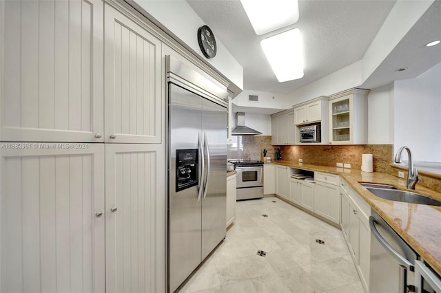 kitchen featuring decorative backsplash, wall chimney exhaust hood, sink, light stone countertops, and appliances with stainless steel finishes