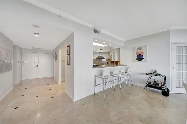 kitchen featuring kitchen peninsula, a breakfast bar area, white cabinetry, crown molding, and wall chimney exhaust hood