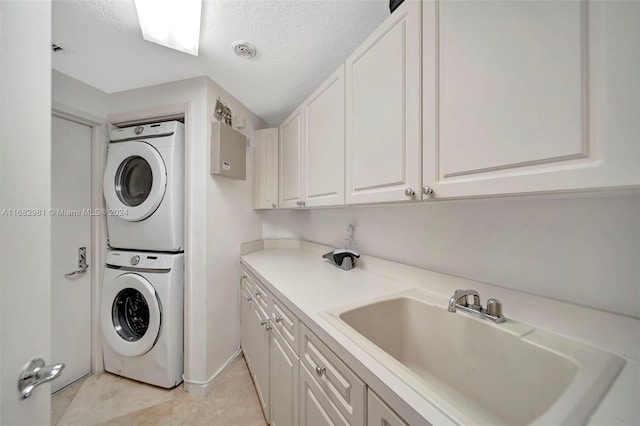 laundry area featuring sink, light tile patterned floors, stacked washer / dryer, a textured ceiling, and cabinets