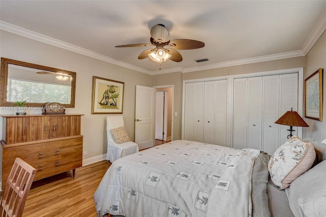 bedroom with light hardwood / wood-style flooring, ceiling fan, crown molding, and two closets