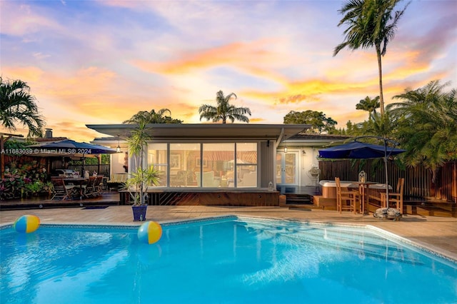 pool at dusk featuring a sunroom and a patio area