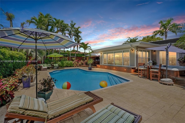 pool at dusk with a patio and a sunroom