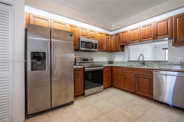 kitchen featuring light stone countertops, a textured ceiling, appliances with stainless steel finishes, and sink