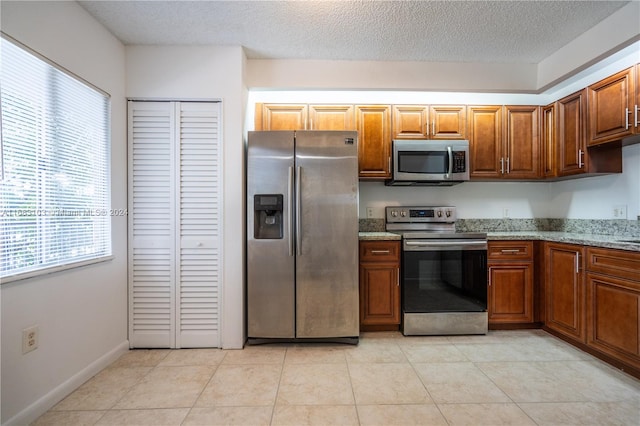 kitchen featuring a textured ceiling, light stone countertops, stainless steel appliances, and light tile patterned floors