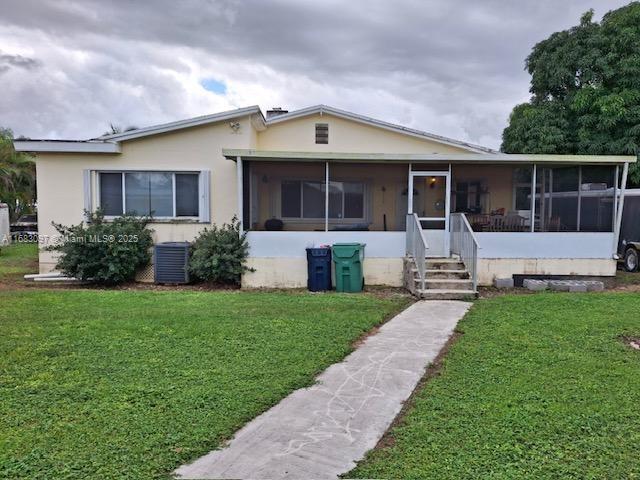 view of front of home with a sunroom, cooling unit, and a front lawn