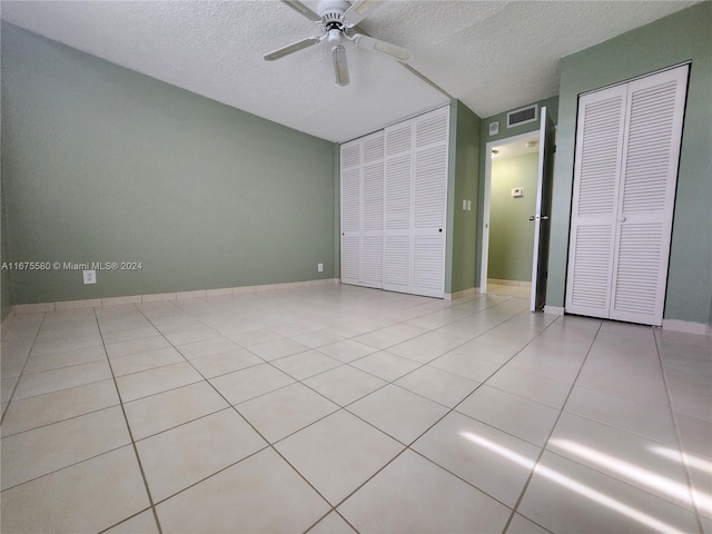 unfurnished bedroom featuring ceiling fan, a textured ceiling, light tile patterned floors, and two closets