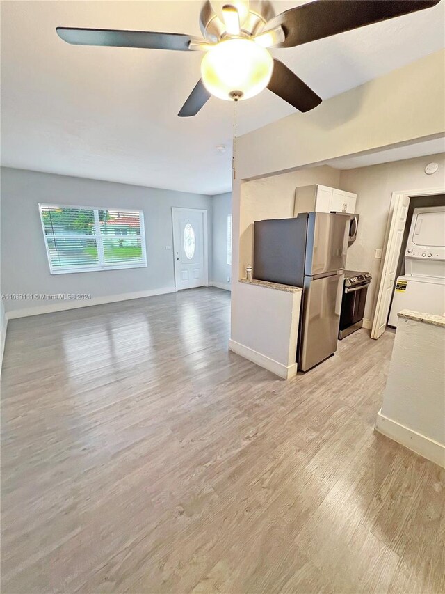 unfurnished living room with ceiling fan, light hardwood / wood-style flooring, and stacked washer and clothes dryer