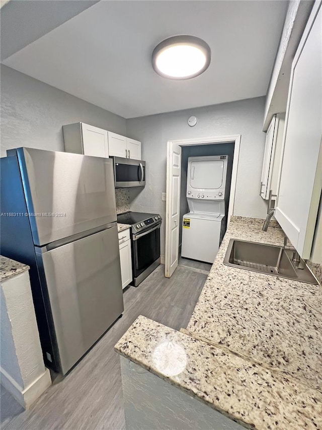 kitchen featuring stacked washing maching and dryer, stainless steel appliances, light stone countertops, light wood-type flooring, and white cabinetry