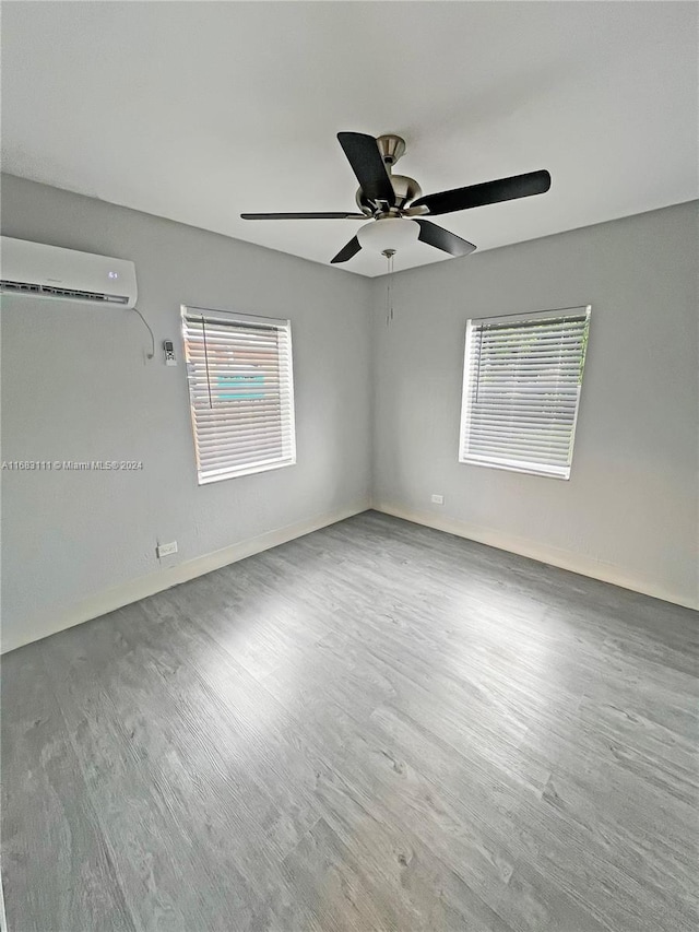 empty room with a wall mounted air conditioner, hardwood / wood-style flooring, and ceiling fan