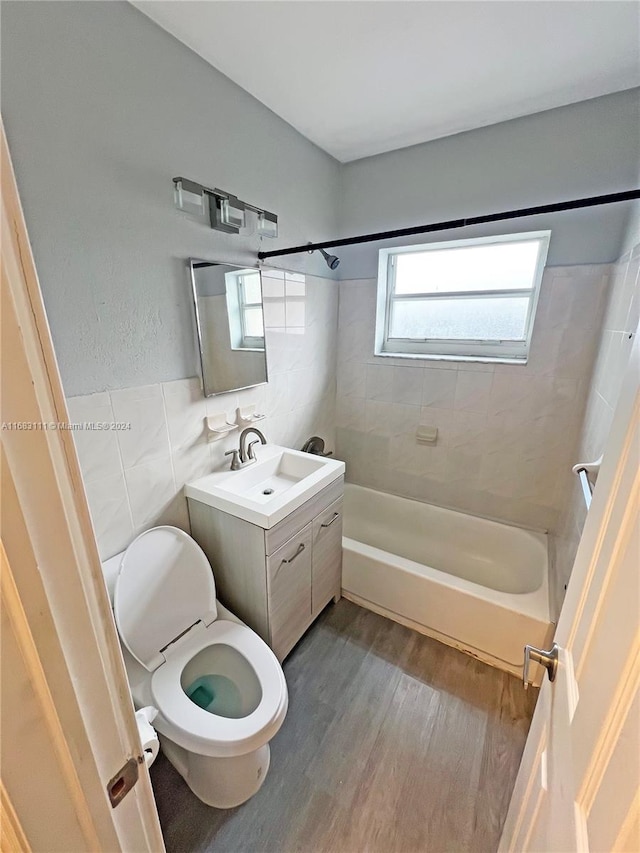 full bathroom with toilet, wood-type flooring, vanity, tiled shower / bath combo, and tile walls