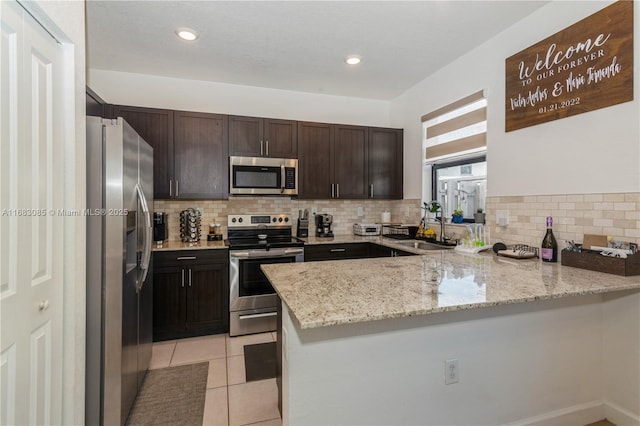 kitchen featuring light tile patterned flooring, sink, kitchen peninsula, stainless steel appliances, and light stone countertops