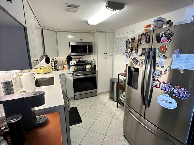 kitchen with appliances with stainless steel finishes, white cabinetry, light tile patterned flooring, and sink