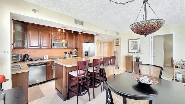 kitchen featuring stainless steel appliances, a textured ceiling, light tile patterned floors, a kitchen island, and a notable chandelier